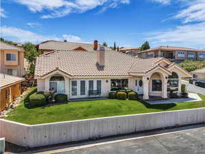 Rear view of house featuring a chimney, a tile roof, stucco siding, a lawn, and a residential view