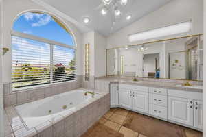 Full bath featuring a ceiling fan, double vanity, a whirlpool tub, vaulted ceiling, and healthy amount of natural light