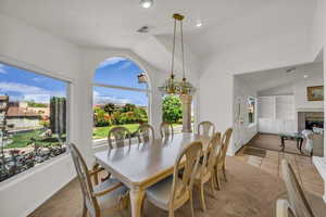 Dining area with built in shelves, light carpet, lofted ceiling, a fireplace, and a chandelier
