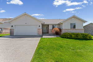 Single story home with a garage, concrete driveway, brick siding, a front lawn, and stucco siding