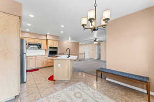 Kitchen with light wood finish cabinets, light carpet, an island with sink, light countertops, and a ceiling fan