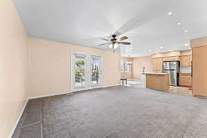 Unfurnished living room with hanging lights, light carpet, ceiling fan, and a textured ceiling