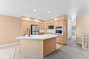 Kitchen with light countertops, light wood finish cabinetry, stainless steel appliances, light tile patterned flooring, and an island with sink