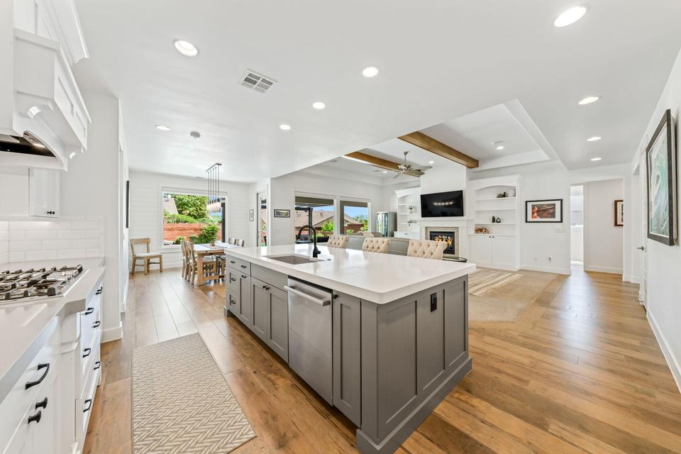 Kitchen with dual tone cabinets, open floor plan, light wood-type flooring, a warm lit fireplace, and an island with sink