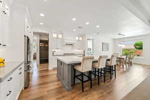 Two tone kitchen featuring a breakfast bar area, an island with sink, light wood-style floors, freestanding refrigerator, and two tone cabinetry