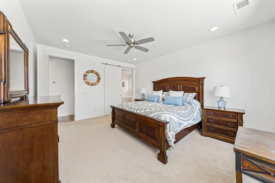 Bedroom with light carpet, a barn door, ceiling fan, recessed lighting, and ensuite bathroom