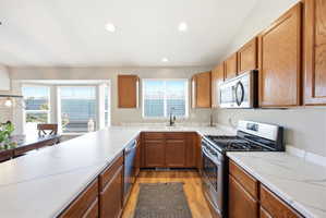 Kitchen featuring stainless steel appliances, wood finish cabinets, light countertops, light wood-style flooring, and recessed lighting