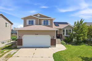 View of front of home featuring brick siding, driveway, solar panels, and a garage