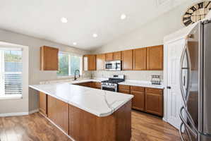 Kitchen with wood finish cabinets, stainless steel appliances, a peninsula, light countertops, and vaulted ceiling