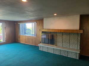 Unfurnished living room with wood walls, carpet floors, a fireplace, and recessed lighting