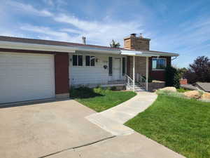 Ranch-style home featuring a front lawn, driveway, a porch, a chimney, and a garage
