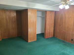 Unfurnished bedroom featuring dark colored carpet, a closet, wood walls, and a ceiling fan