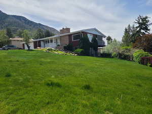 View of home's exterior with an attached garage, a chimney, a yard, brick siding, and a mountain view