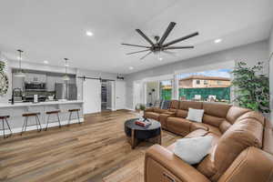 Living room featuring a barn door, light wood-style flooring, a ceiling fan, and recessed lighting