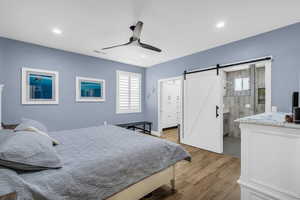 Bedroom featuring a barn door, light wood-style flooring, a spacious closet, a ceiling fan, and ensuite bathroom