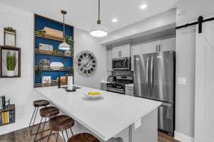 Kitchen with a kitchen bar, a peninsula, stainless steel appliances, a barn door, and open shelves