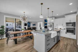 Two tone kitchen with a center island with sink, a chandelier, ceiling fan, light wood-style floors, and decorative backsplash
