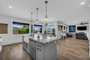 Kitchen featuring light stone countertops, light wood-style flooring, a center island with sink, and open floor plan