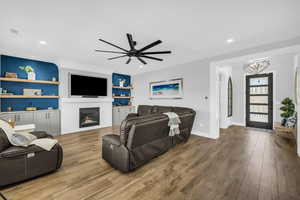 Living room featuring built in shelves, a ceiling fan, wood finished floors, and a glass covered fireplace