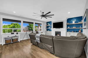 Living area featuring a ceiling fan, wood finished floors, a glass covered fireplace, and built in shelves