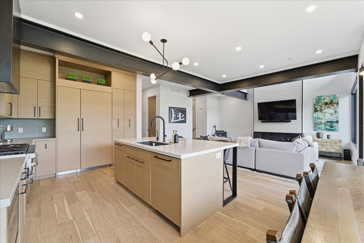 Kitchen with light wood finish cabinets, a kitchen island with sink, open shelves, and light wood-type flooring