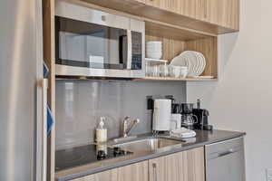 Bar featuring stainless steel appliances, light wood finish cabinetry, modern cabinets, dark stone counters, and open shelves