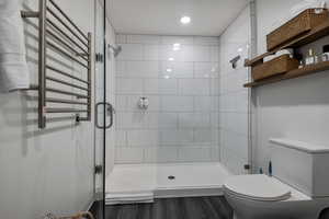 Bathroom featuring a towel warming rack, radiator heating unit, a shower stall, and dark wood-style floors