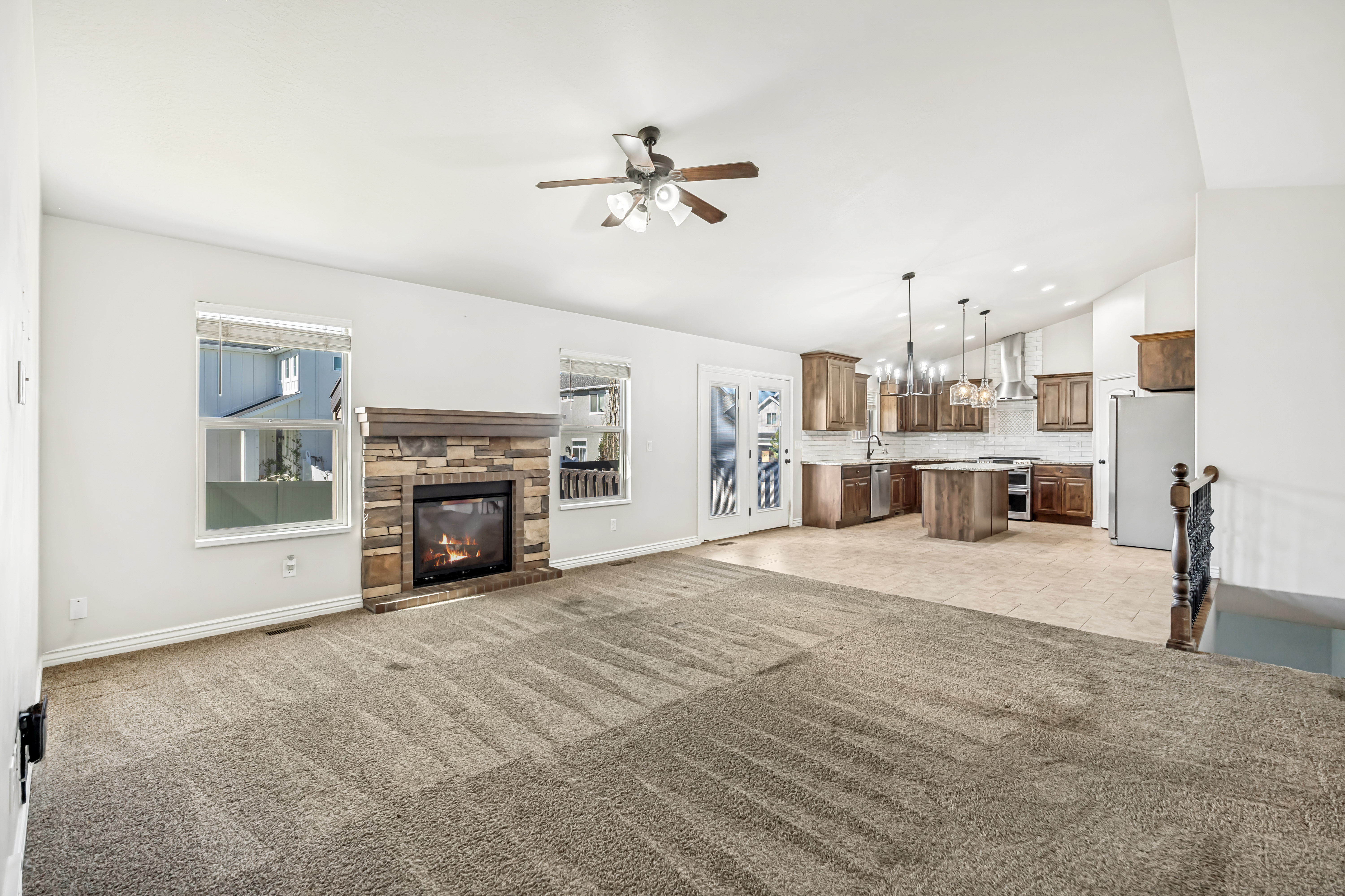 Unfurnished living room featuring ceiling fan, vaulted ceiling, a fireplace, light carpet, and a chandelier