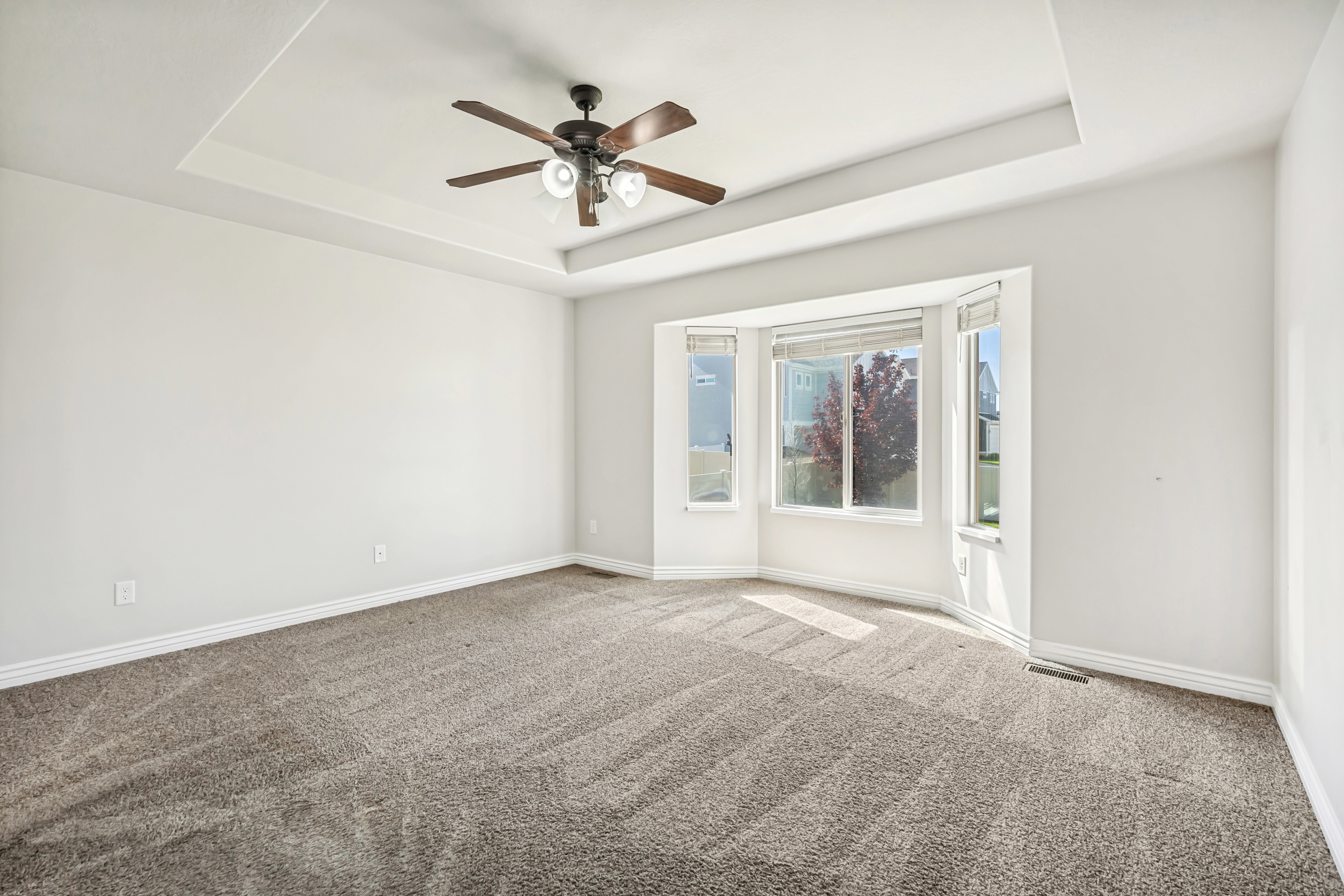 Unfurnished room featuring ceiling fan, light colored carpet, and a raised ceiling