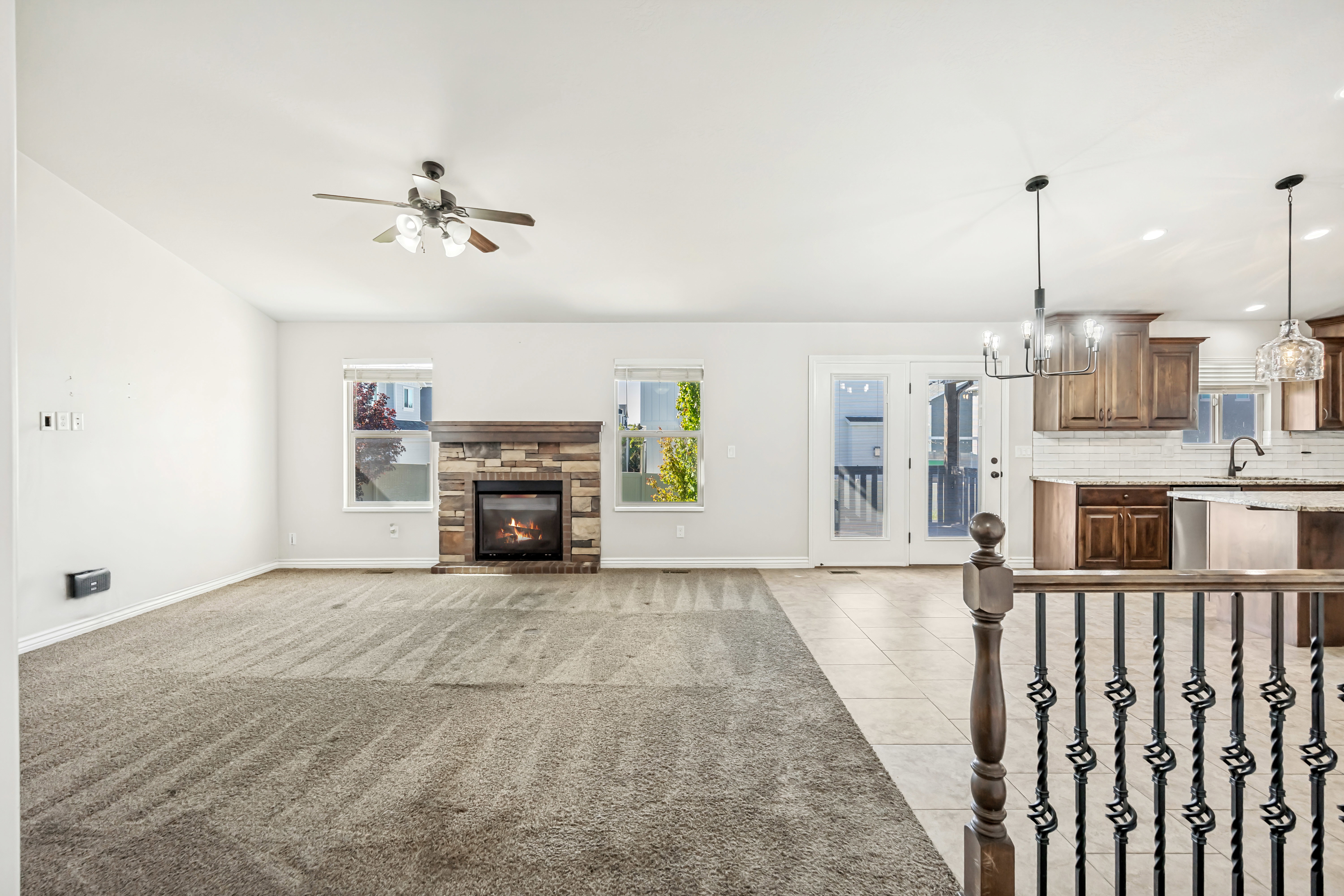 Unfurnished living room with hanging lights, a stone fireplace, light tile patterned flooring, and ceiling fan