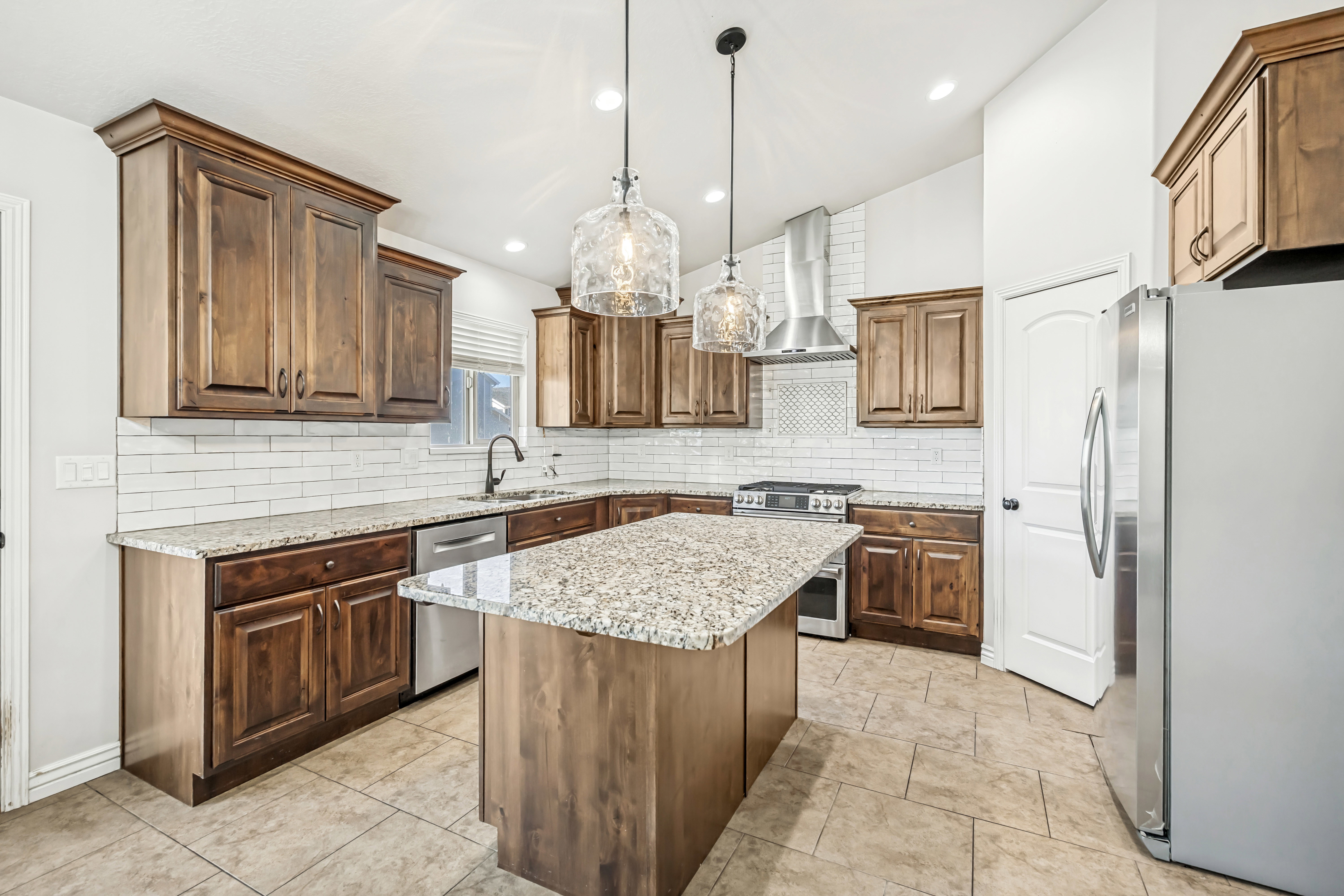 Kitchen with stainless steel appliances, a kitchen island, light stone countertops, pendant lighting, and tasteful backsplash