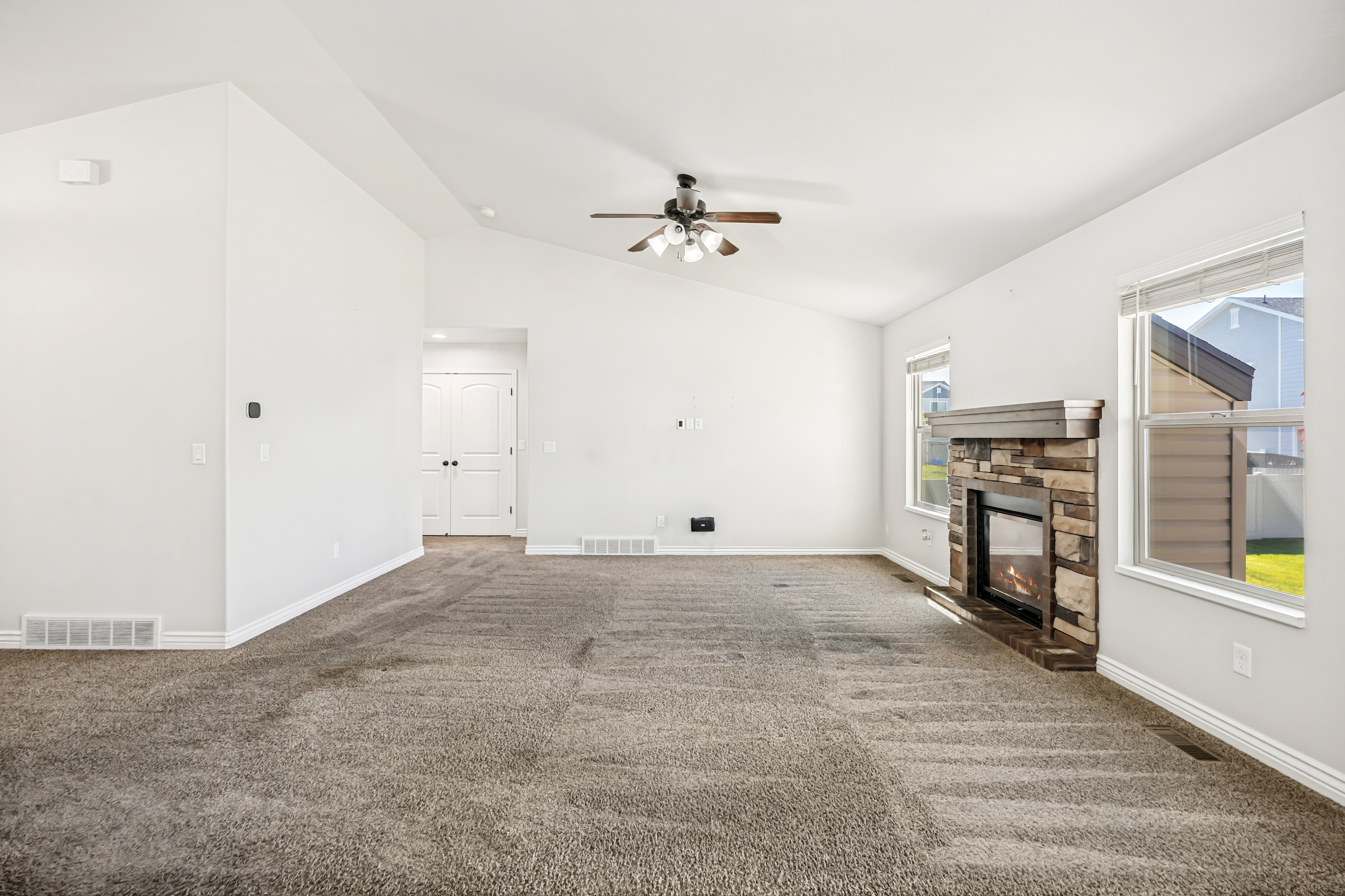 Unfurnished living room with dark colored carpet, a ceiling fan, a fireplace, and vaulted ceiling