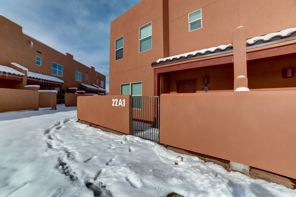 View of snowy exterior with stucco siding, a gate, and a tiled roof