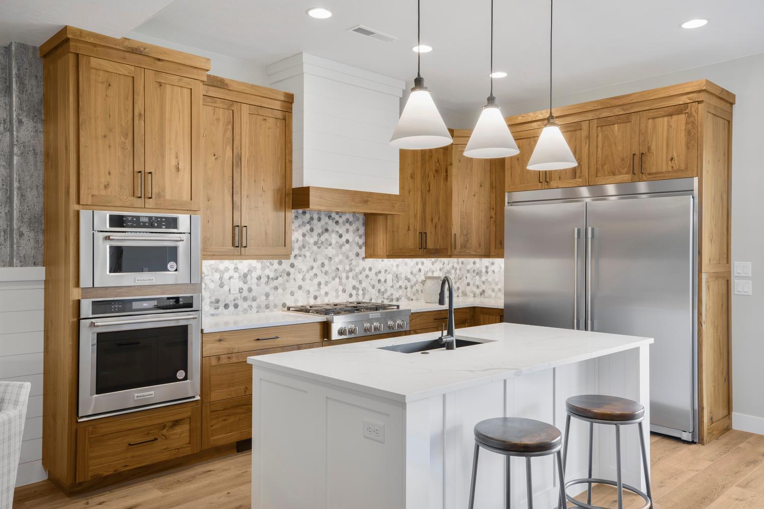 Kitchen with stainless steel appliances, dual tone cabinets, light stone countertops, a kitchen island with sink, and a kitchen breakfast bar
