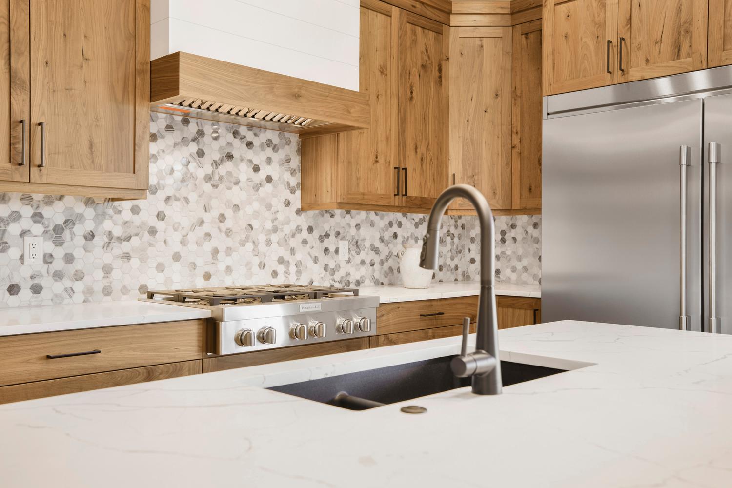 Kitchen with stainless steel appliances, light stone countertops, backsplash, and wood finish cabinets