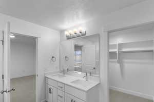 Full bathroom featuring a walk in closet, double vanity, light carpet, and a textured ceiling