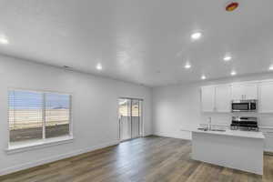 Kitchen featuring white cabinets, stainless steel appliances, dark wood-style flooring, an island with sink, and recessed lighting