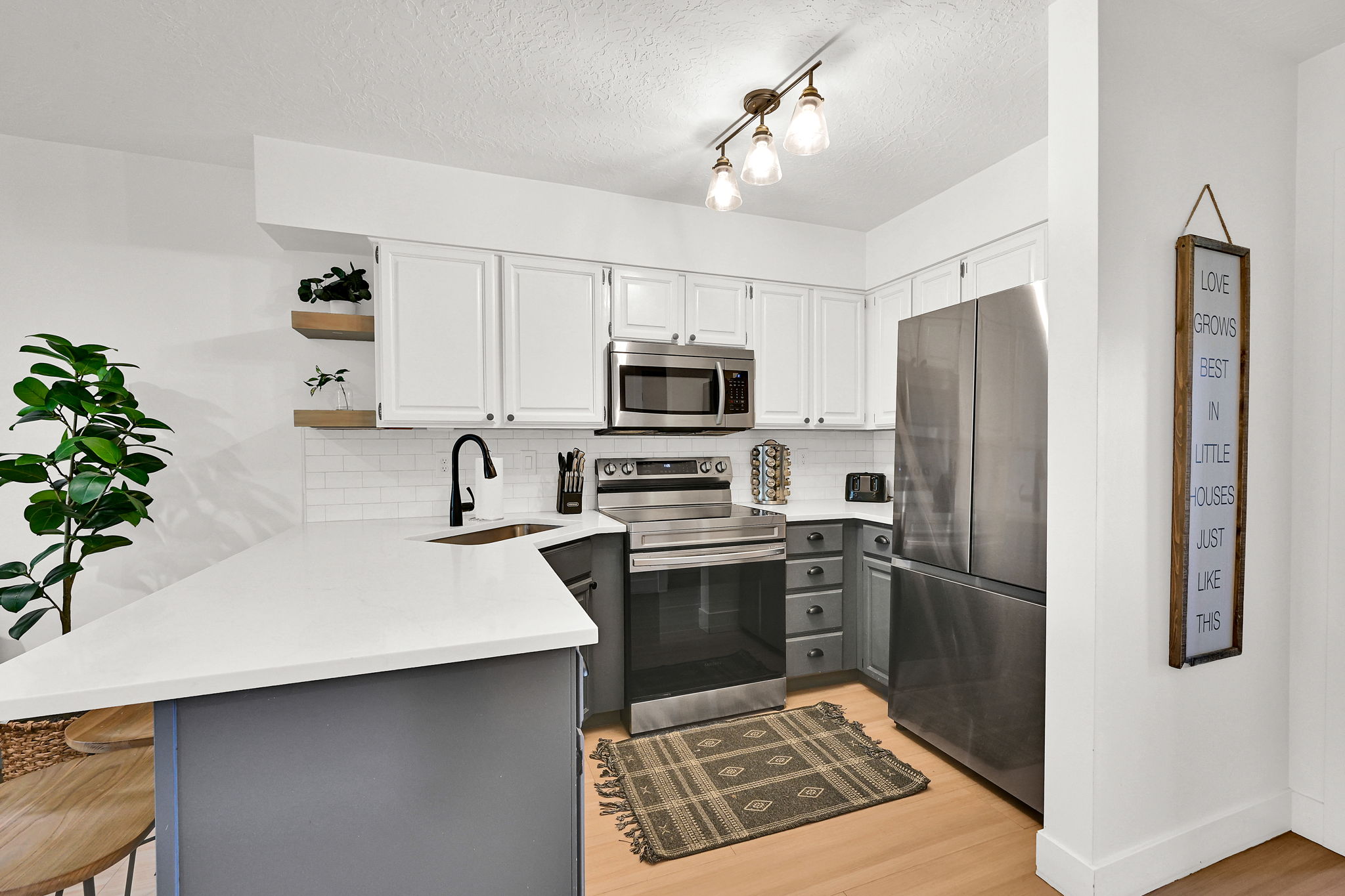 Kitchen featuring a peninsula, a breakfast bar, open shelves, stainless steel appliances, and two-tone cabinets.
