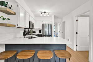 Kitchen featuring a peninsula, a breakfast bar, open shelves, stainless steel appliances, and two-tone cabinets.