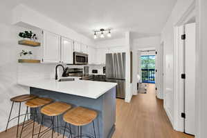 Kitchen featuring a peninsula, a breakfast bar, open shelves, stainless steel appliances, and two-tone cabinets.