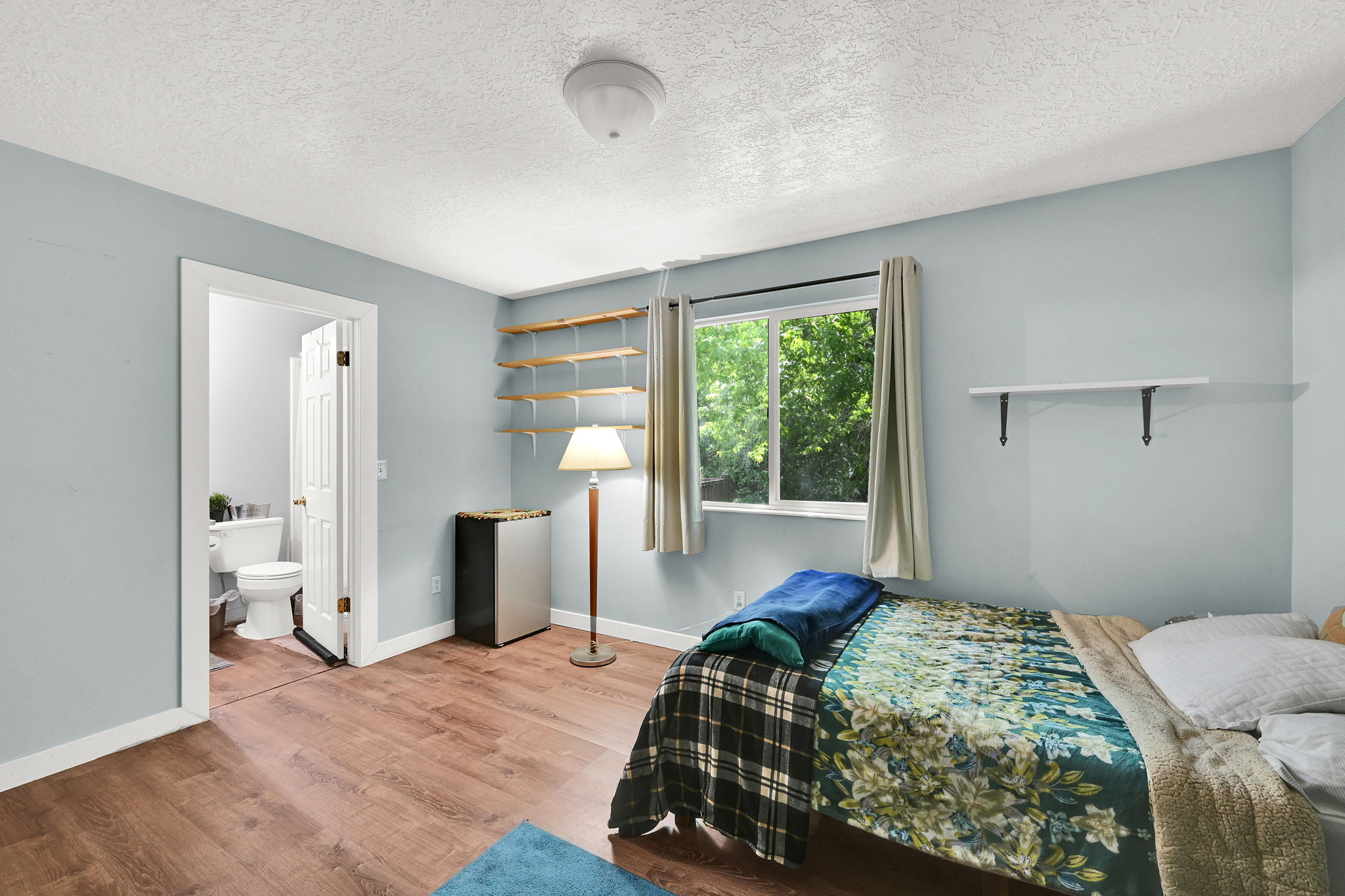 Bedroom featuring freestanding refrigerator, light wood-type flooring, a textured ceiling, and connected bathroom