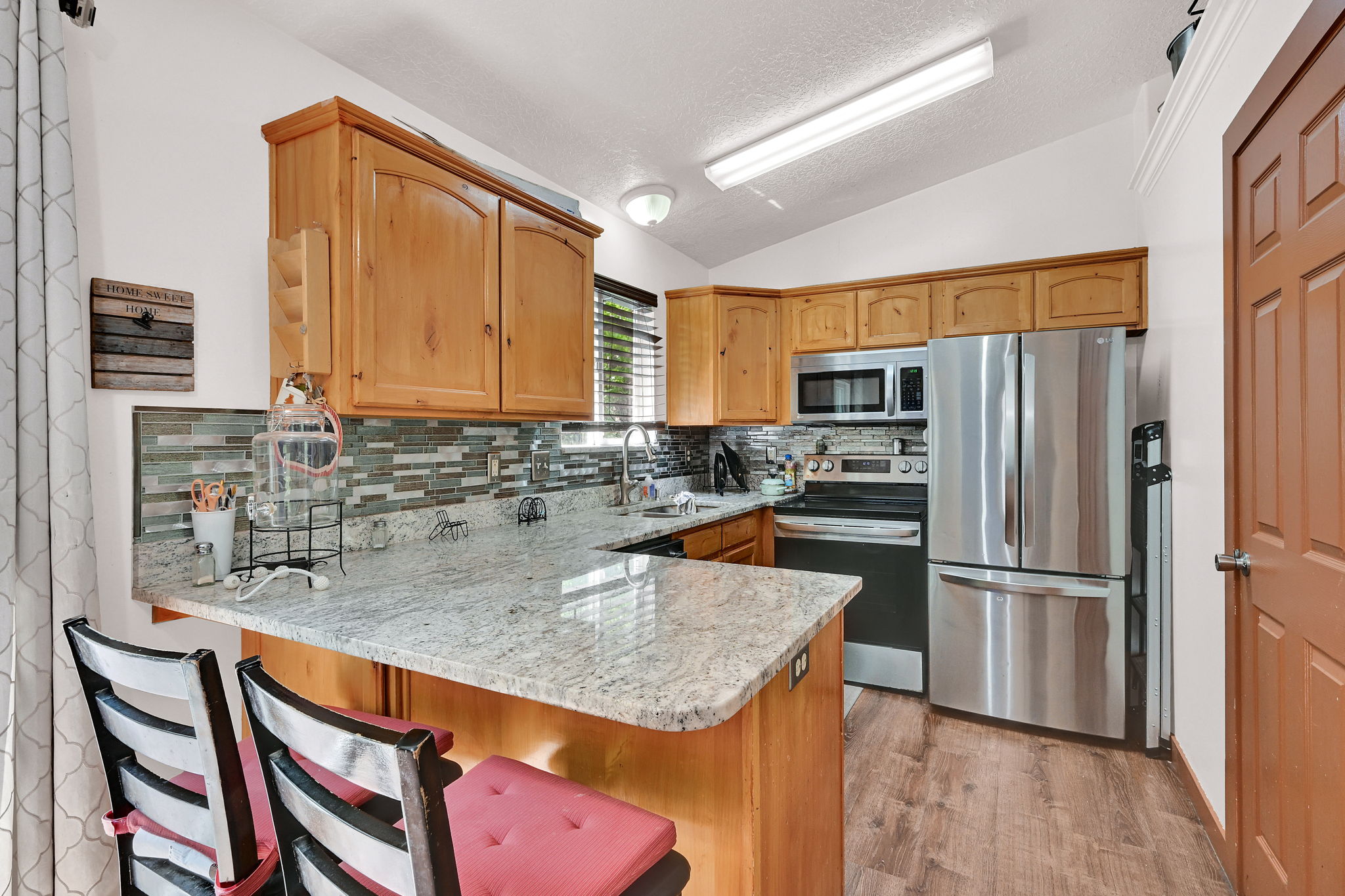 Kitchen featuring a peninsula, light stone countertops, stainless steel appliances, a breakfast bar, and light wood-style floors