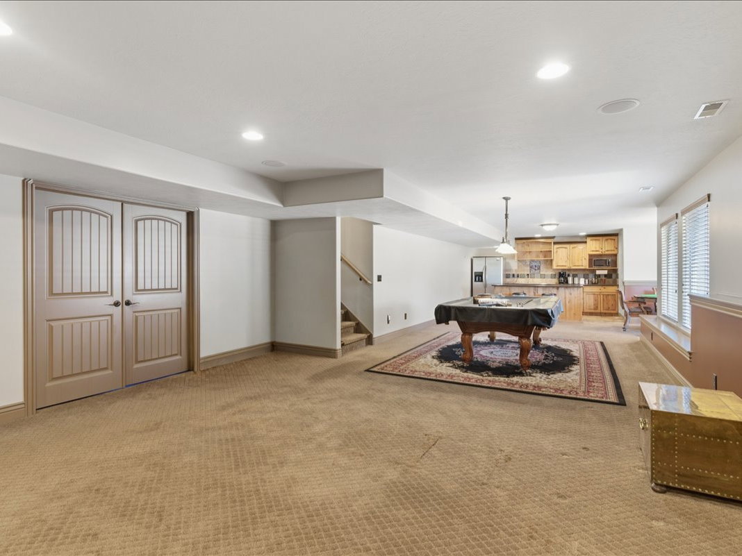 Spacious lower-level area with recessed lighting, light wood paneled double doors, a built-in wet bar with light wood cabinetry, and a carpeted floor