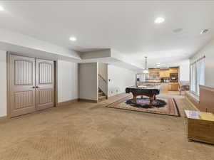 Spacious lower-level area with recessed lighting, light wood paneled double doors, a built-in wet bar with light wood cabinetry, and a carpeted floor