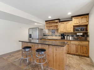 Kitchenette featuring knotty wood cabinetry, dark countertops, a tile backsplash, and a built-in island with seating space