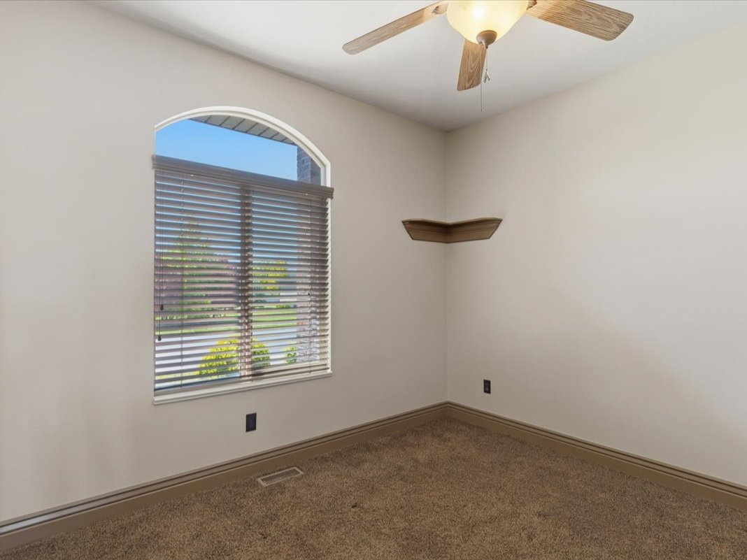 Arched window with blinds, ceiling fan, corner shelving, neutral wall color, and carpeted flooring