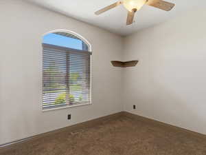 Arched window with blinds, ceiling fan, corner shelving, neutral wall color, and carpeted flooring