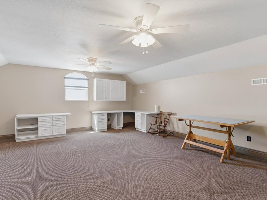Spacious room featuring carpeting, two ceiling fans, built-in white cabinetry, a built-in white desk with drawers, and an arched window