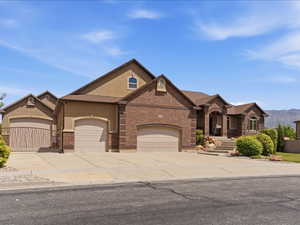 Spacious residence featuring a brick and stucco exterior, multiple garage bays with arched entrances, a covered entry porch with columns, a terraced front walkway, and mature landscaping