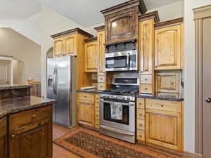 Kitchen featuring stainless steel appliances, wood cabinetry, stone countertops, a tile backsplash, and wood-finish flooring